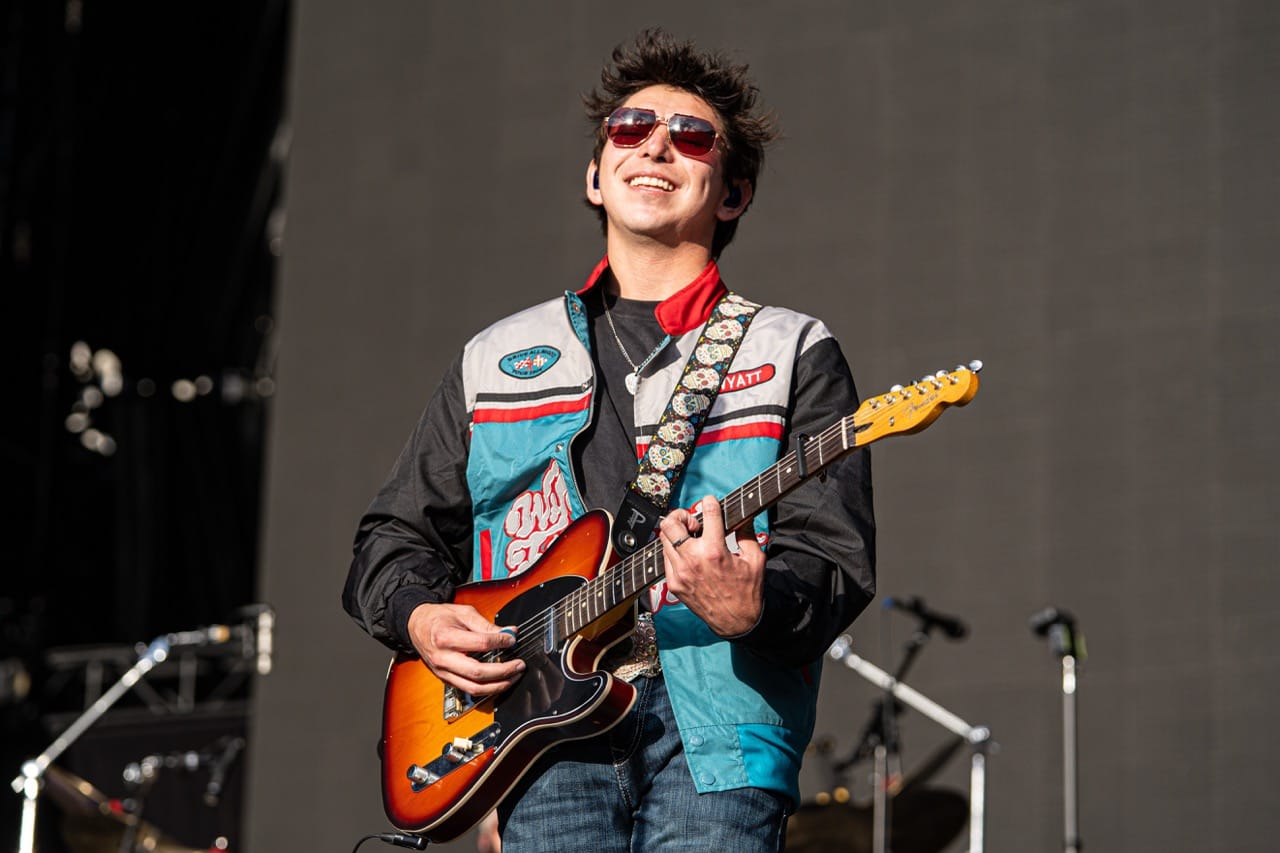 Wyatt Flores smiles while playing guitar on stage at Boone Pickens Stadium in Stillwater on April 11, 2026, wearing a racing-style jacket with his name on the chest.