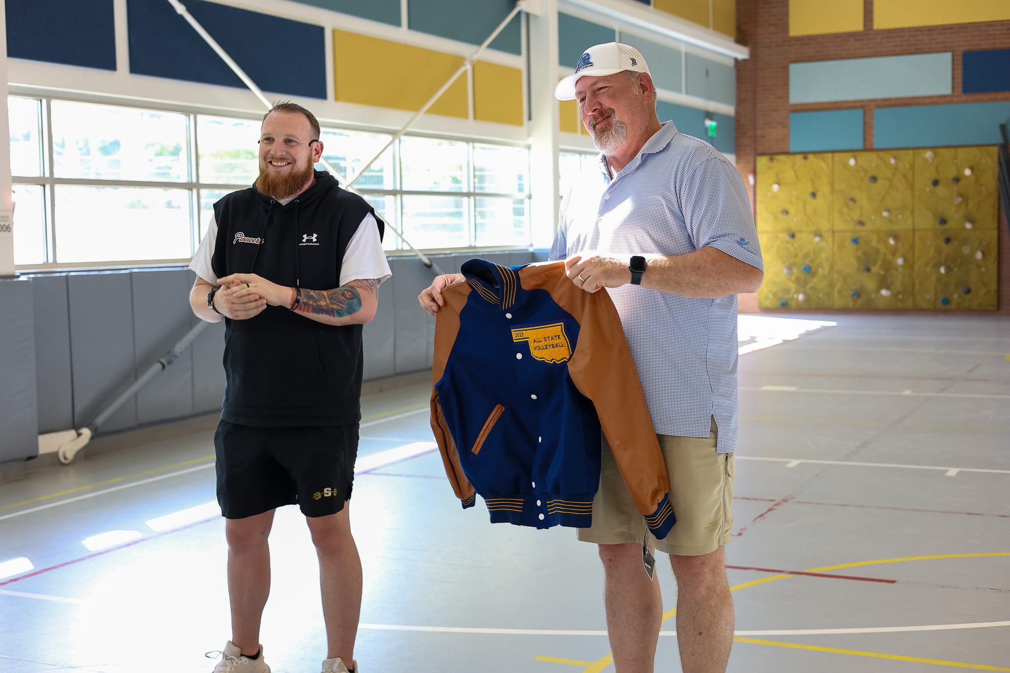 Stillwater volleyball coach Andrue Brown and booster club member Jake Fahlenkamp display Taylor Rattay's All State jacket at Will Rogers Elementary on May 12, 2026. 