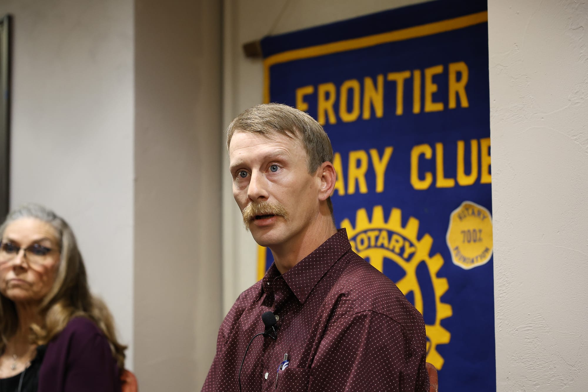 Clayton Estus speaks at the Stillwater Frontier Rotary Club candidate forum on May 28, 2026, in Stillwater, with incumbent Commissioner Rhonda Markum visible at left.
