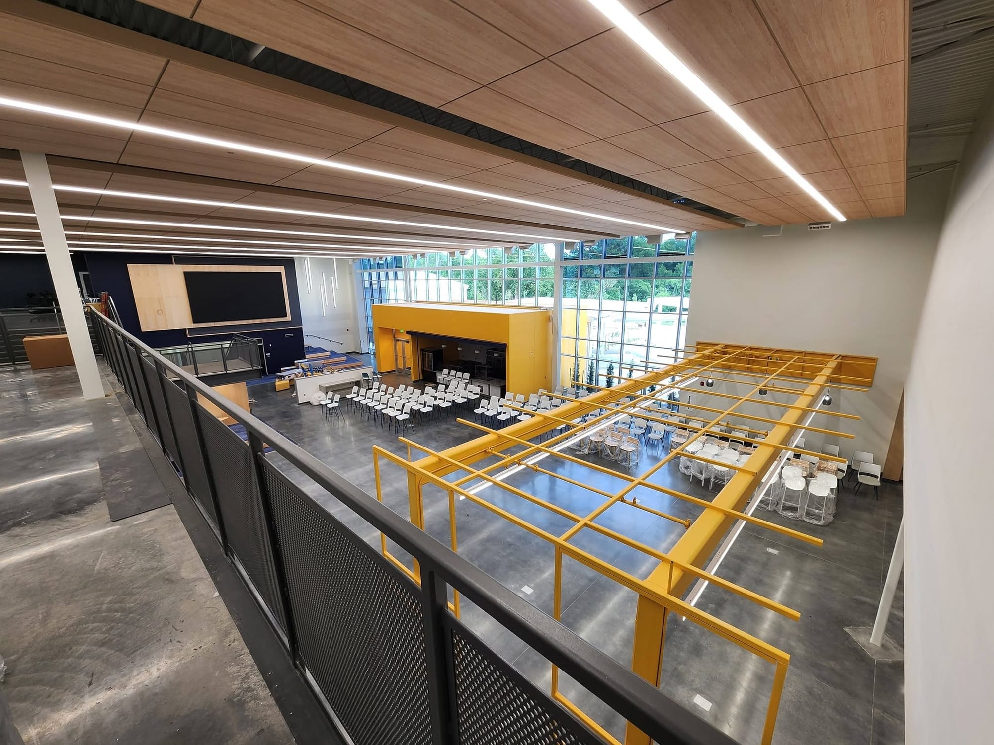 An overhead view of the new Stillwater High School student center shows rows of white chairs, gold structural framework, a large display screen and floor-to-ceiling windows.