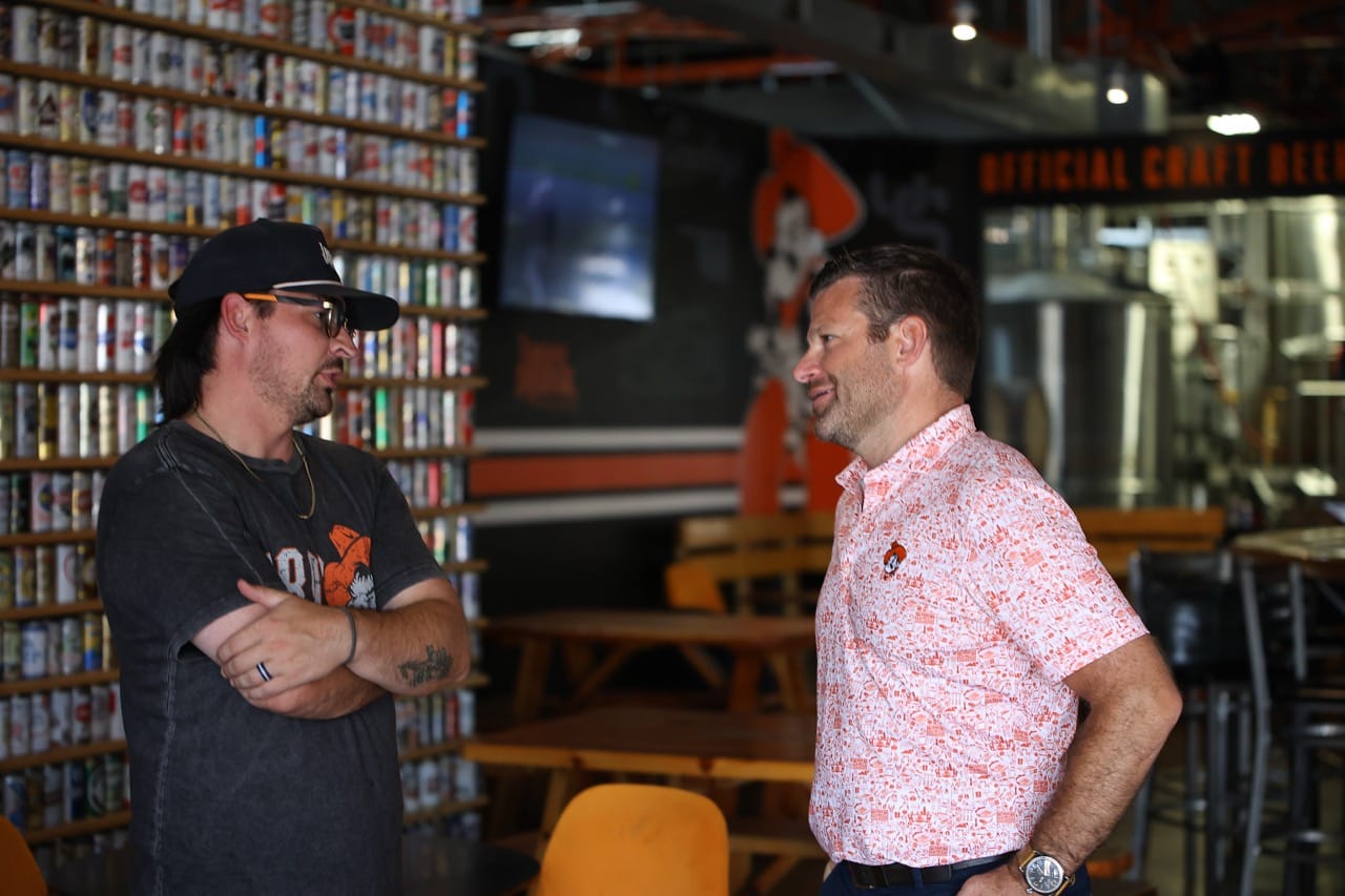 Trenton Inselman, left, talks with Brady Sidwell inside Iron Monk Brewing Company's taproom, in front of the wall of beer cans and a TV.