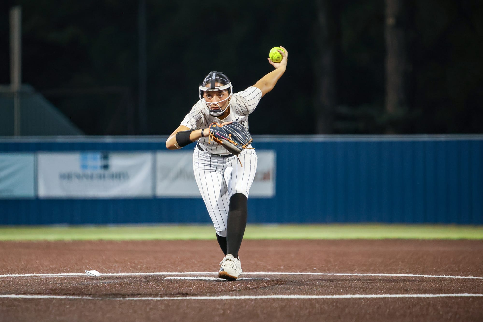 Stillwater junior Grace Tonga, wearing a face mask, winds up to deliver a pitch during a night softball game against Guthrie on Sept. 28, 2026, at Couch Park in Stillwater.