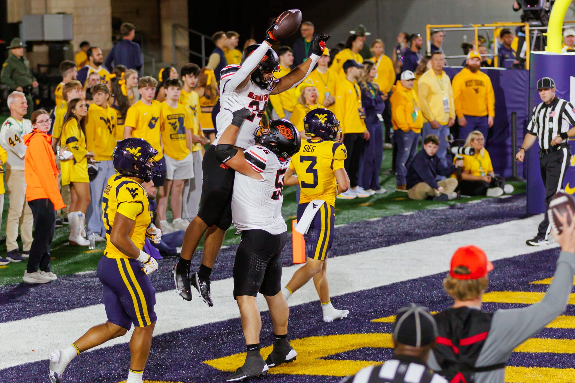 Oklahoma State offensive lineman Tyler Mercer, No. 56, lifts running back Caleb Hawkins, No. 24, who holds the football overhead in the end zone.