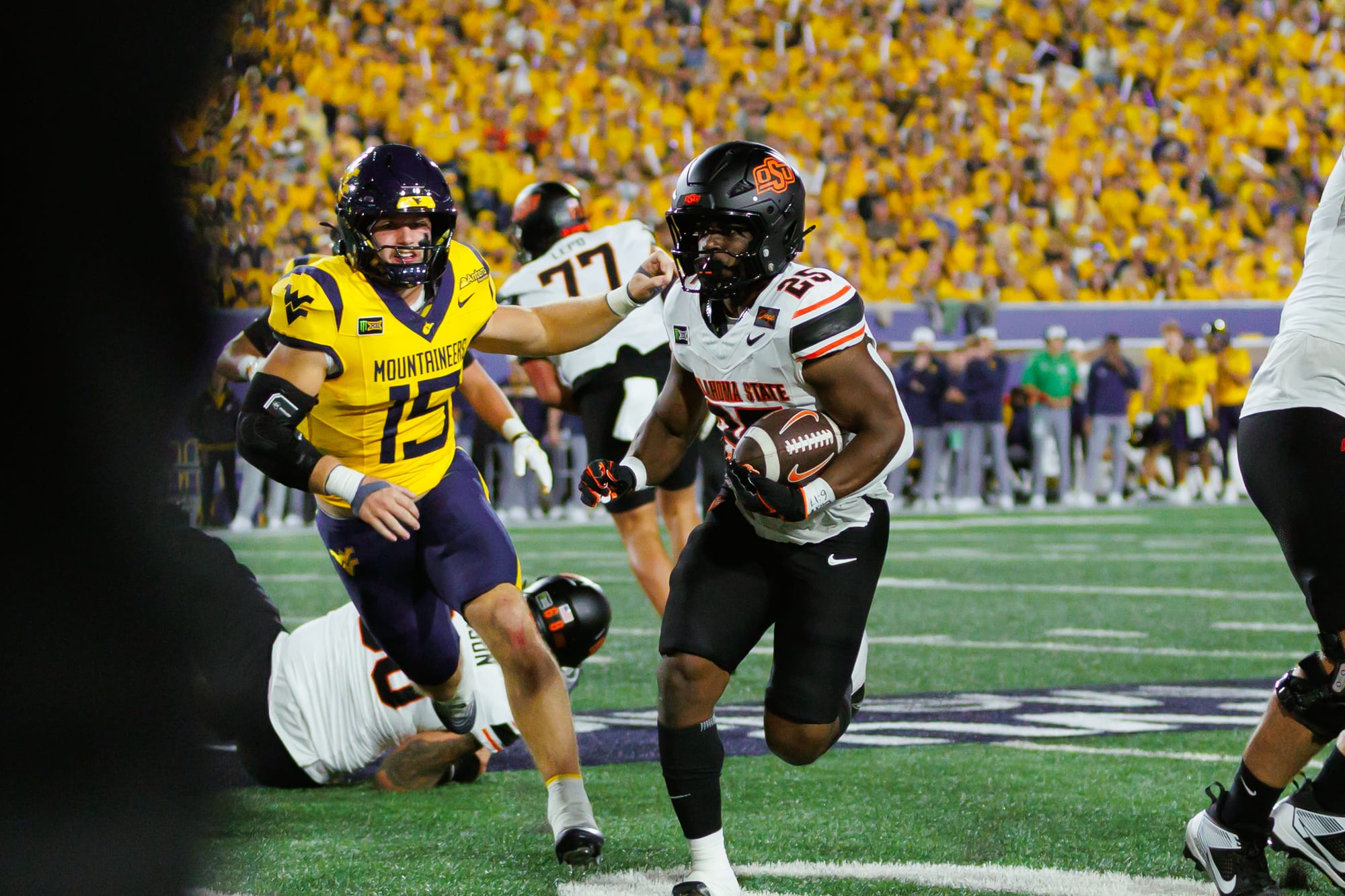 Oklahoma State running back Ayo Adeyi, No. 25, runs with the football as West Virginia linebacker Ben Cutter, No. 15, reaches toward him.