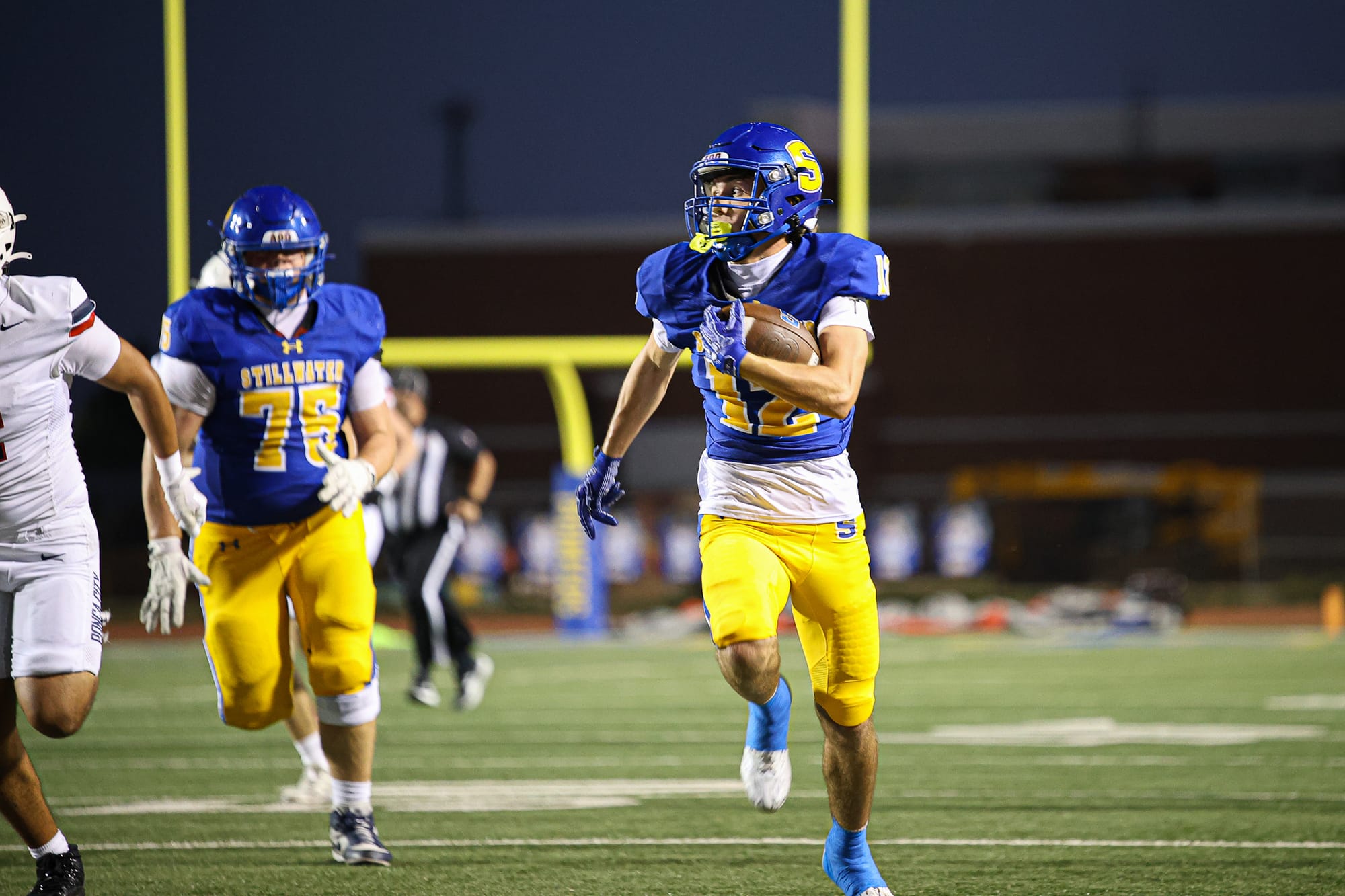 Stillwater senior Peyton Campbell (12) carries the ball upfield on a 65-yard touchdown catch against Ponca City at Pioneer Stadium as teammate Roddy Spatz (75) trails.