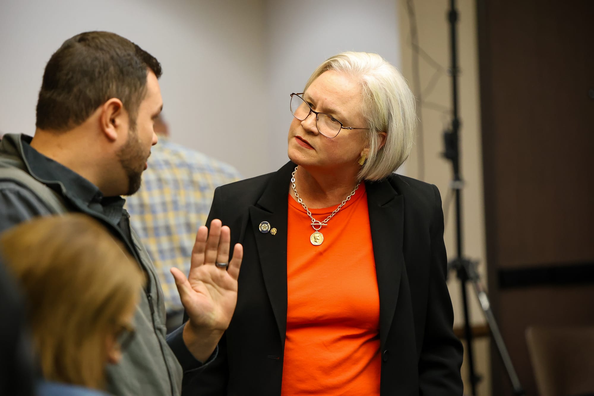 Rep. Trish Ranson, in a black blazer and orange top, listens as a man in a gray vest gestures while talking with her at a Stillwater Rotary Club forum on Oct. 22, 2026.