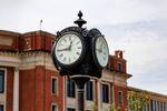 The Payne County centennial clock, labeled "Payne County" and "Stillwater," stands in downtown Stillwater with a red brick county courthouse in the background.