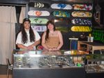 Ivan Serrano, left, and Isa Edge smile behind the glass display counter at i&i Skateshop in Stillwater, with skate decks mounted on the wall behind them.