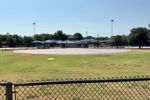 Empty concrete infield pad at a Strickland Park ballfield in Stillwater, with dugouts, light poles and a chain-link fence in the foreground.