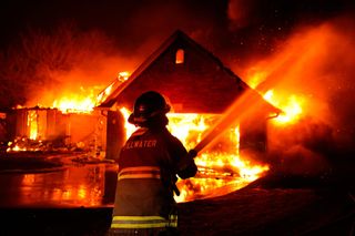 Stillwater firefighter silhouetted against a home fully engulfed in flames during the March 14, 2025 wildfire in the Pecan Hill neighborhood.