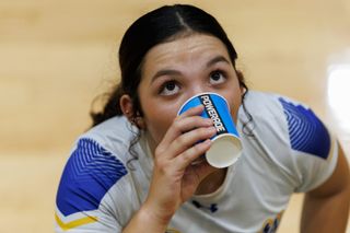 A closeup photo of a volleyball player drinking out of a powerade branded cup with eyes looking up
