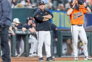 Oklahoma State head coach Josh Holliday stands with arms crossed near the dugout during the Shriners College Showdown at Globe Life Field in 2025.