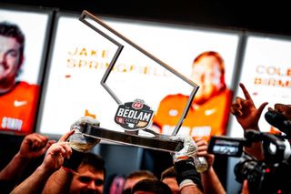 Hands hold up the Bedlam Series trophy featuring the rivalry's logo after Oklahoma State's 27-24 victory over Oklahoma in the final Bedlam football game November 2023