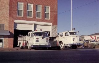 Two white fire department pumper trucks parked outside brick Fire Station Number One building in downtown Stillwater in January 1963