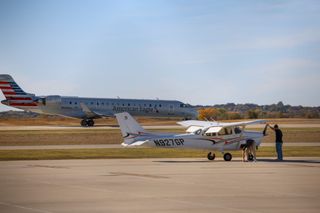 An American Eagle regional jet taxis behind a general aviation plane and two people preparing it on the tarmac at Stillwater Regional Airport on Nov. 7, 2025.