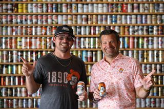 Trenton Inselman, left, holds a can of Enid Brewing's Cowboy Blonde and Brady Sidwell holds a can of Iron Monk's Original 1890 in front of the taproom's wall of beer cans.