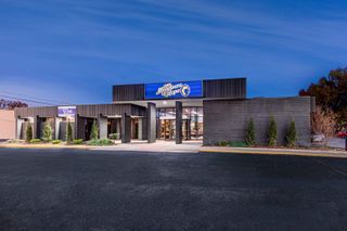 A modern, single-story building with a dark facade and a blue "Lions Meadows of Hope" sign above the entrance, photographed at dusk with a clear blue sky.