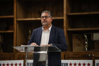 Kevin Wright speaks from a lectern at a Republican candidate event at Oak Grove Public School in Cushing, campaign signs bearing his name lining the front.