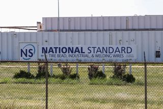 A sign reading "National Standard: Tire Bead, Industrial, and Welding Wires, A Heico Company," outside the company's Stillwater manufacturing plant.