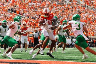 Oklahoma State receiver Justin Bowick in orange jersey number 0 catches a football at the goal line as two Oregon defenders in white and green converge on him at Boone Pickens Stadium.