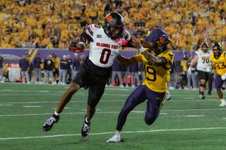 Oklahoma State wide receiver Justin Bowick, No. 0 in a white jersey, stiff-arms a West Virginia defender in gold while carrying the football in front of a packed crowd.