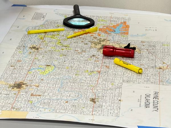 A plat map of Payne County with highlighters, a magnifying glass and a small flashlight.