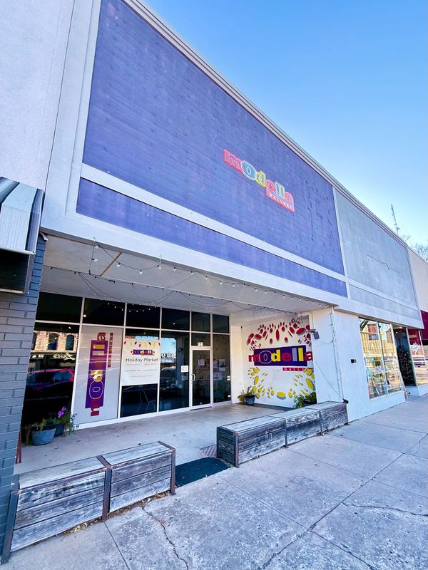 The art gallery's frontage. A Modella gallery neon sign with a faded purple background and front porch area