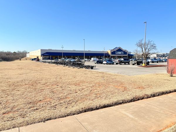 Showing an grassy space with Lowe's Home Center in the background and their parking lot in the foreground.