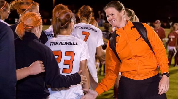 OSU women's soccer coach Karen Hancock in orange jacket shakes hands with players in white uniforms after a match during the 2015 season at Oklahoma State University in Stillwater, Oklahoma.
