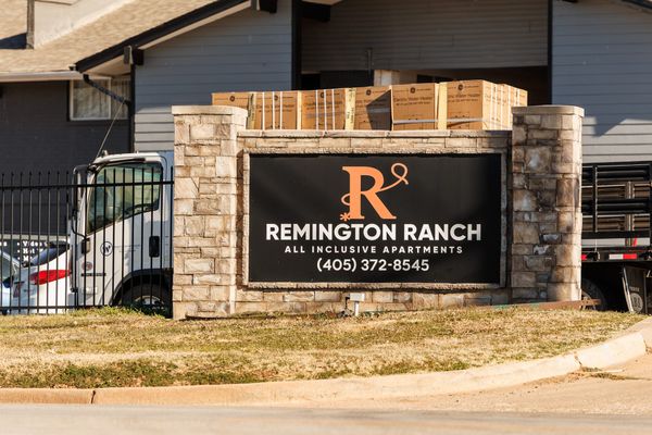 Delivery truck loaded with boxed water heaters parked behind the Remington Ranch apartments entrance sign, which displays the complex name and phone number on a stone pillar structure