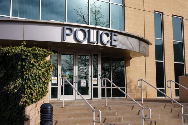 Front entrance of Stillwater Police Department building with tan brick facade, curved POLICE awning over glass doors, metal handrails, and concrete steps
