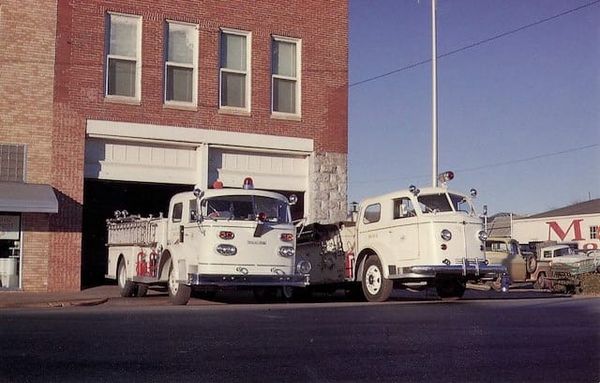 Two white fire department pumper trucks parked outside brick Fire Station Number One building in downtown Stillwater in January 1963