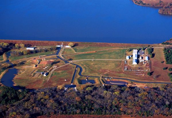 Aerial photo showing Lake Carl Blackwell's earthen dam running along the shoreline, with the USDA Hydraulic Engineering Research Laboratory facility visible below the dam.