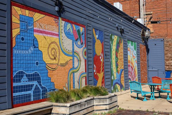 Four colorful student-designed murals on the exterior wall of Chris Salmon Plaza in downtown Stillwater, with a blank panel at right reserved for a new mural to be unveiled April 24.