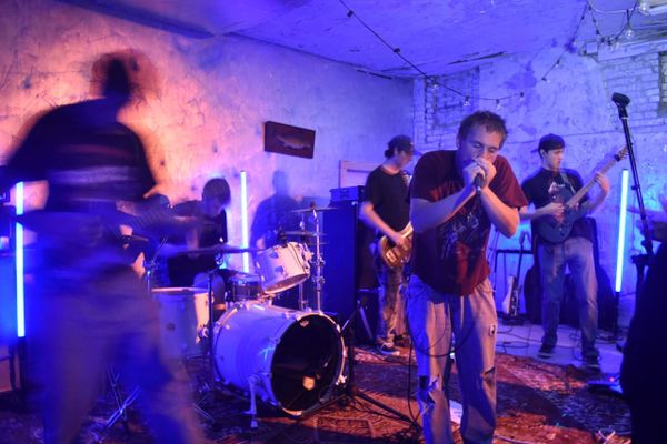 Dreamsickle vocalist Asa Thompson sings into a mic at Velvet Fudge, surrounded by bandmates under blue and pink stage lighting.