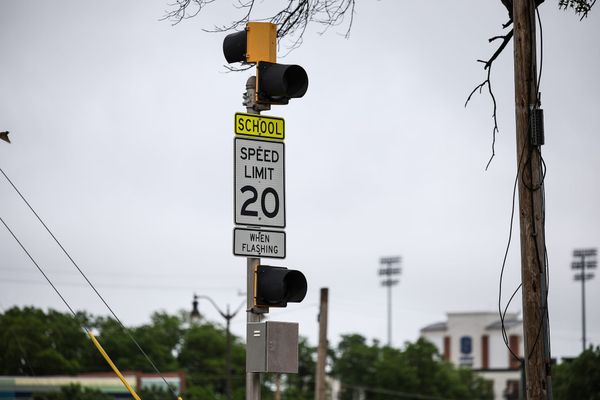 A school zone speed limit sign reading 20 mph when flashing on a Stillwater street, with stadium lights visible in the background.