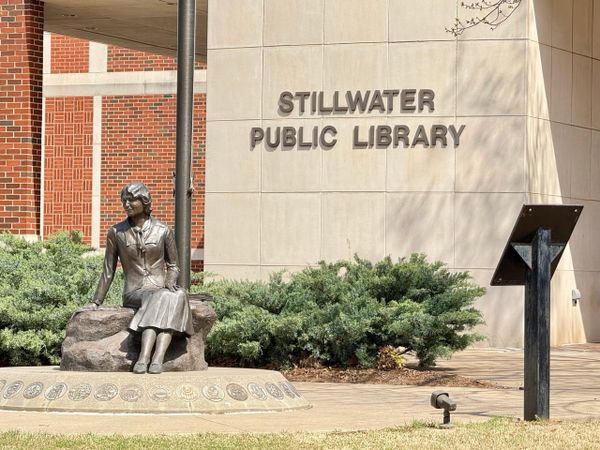 Bronze statue of historian Angie Debo seated outside the Stillwater Public Library on a sunny day in Stillwater, Oklahoma.