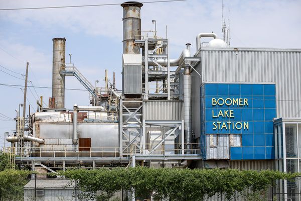 Exterior view of the vacant Boomer Lake Station power plant, a decommissioned natural gas-fired steam turbine facility, showing its rusted smokestacks and blue sign in Stillwater.