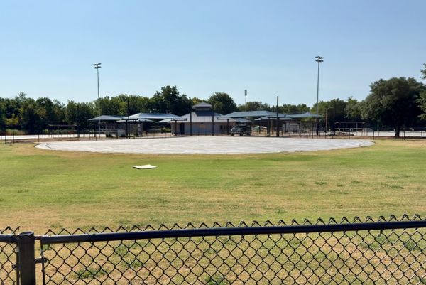 Empty concrete infield pad at a Strickland Park ballfield in Stillwater, with dugouts, light poles and a chain-link fence in the foreground.