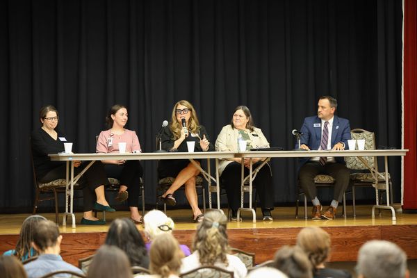 Five panelists seated at a table on a stage during a forum on children and screen use, with one speaking into a microphone as audience members watch from the front rows.