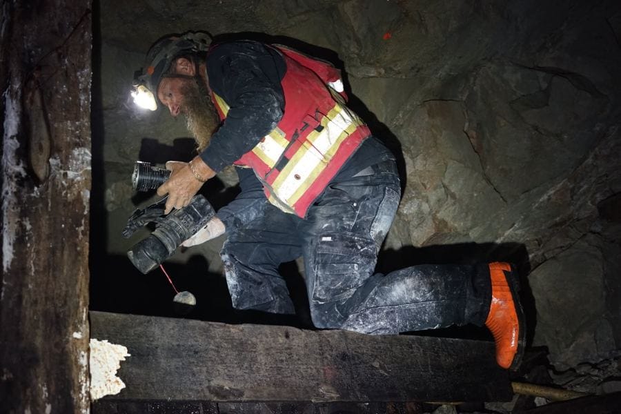Frank Schlichting in a climbing helmet, headlamp lit, checking his gas detector underground