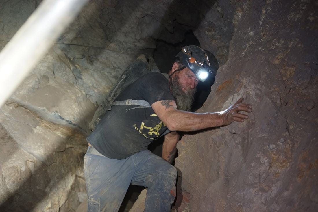 Frank Schlichting crawling through a tight passage in an abandoned BC mine — a frame from the documentary UNDERMINE