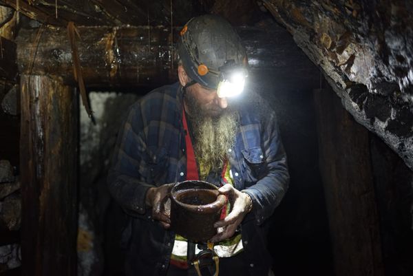 Frank Schlichting in a helmet and headlamp, holding an old rusted pot in both hands in a timbered mine tunnel