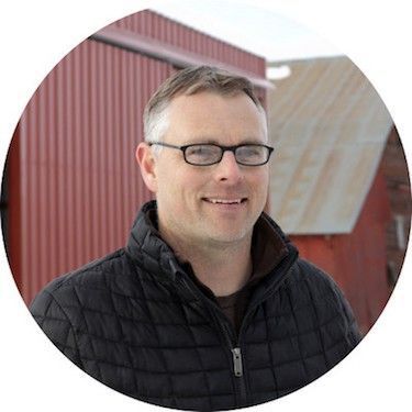 Josh Phifer head shot in front of large, red, metal building. He's smiling.