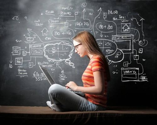 Young woman in an orange striped shirt and glasses working on a laptop.