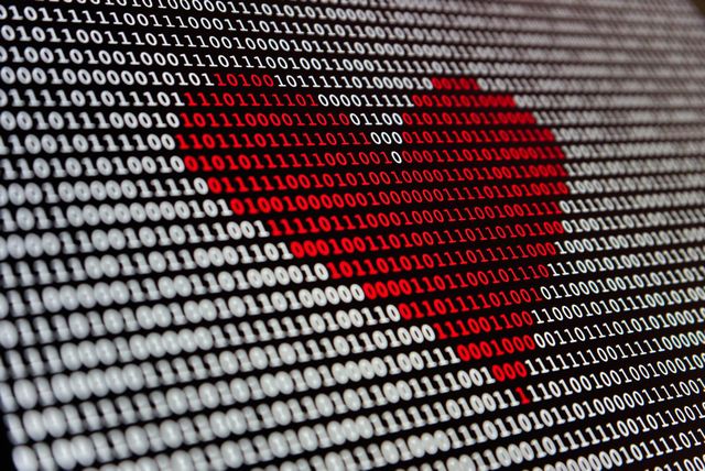 Red heart on computer screen made of binary code.