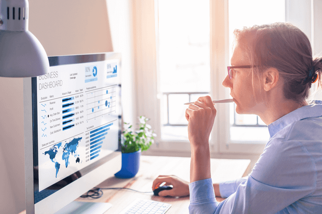 Woman with pen in mouth looking at computer screen. 