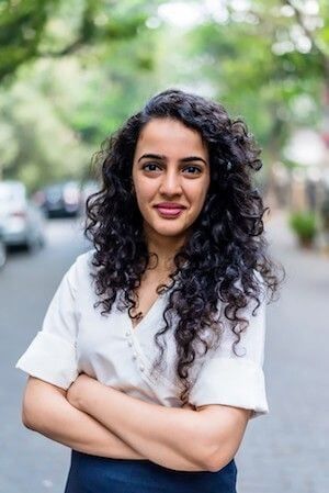 Antaraa V. headshot, dark curly hair, white shirt, crossed arms.