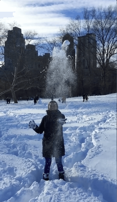 Young woman outside in the winter throwing snow in the air.