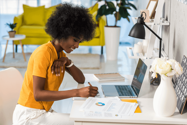 Woman in yellow blouse sitting at desktop in front of laptop.